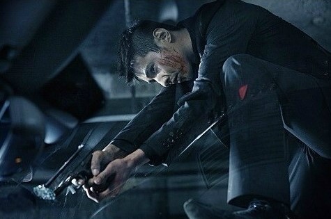 Movie still: a man in a dark suit crouching with a pistol